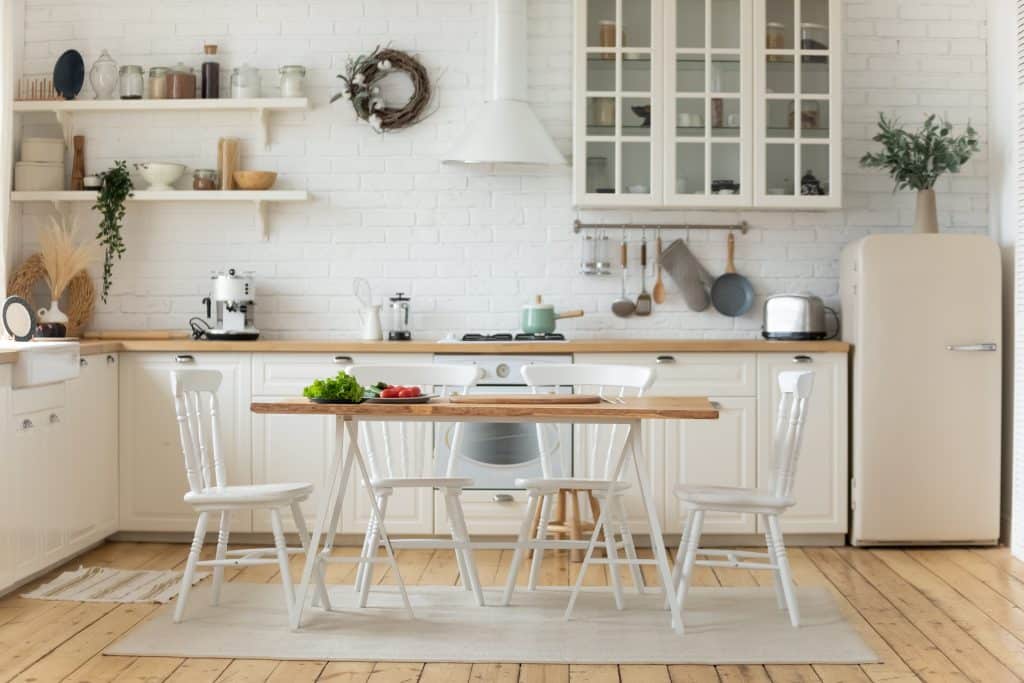 A modern kitchen with a dining table in the middle. Cabinets, floors, shelves, and the table with chairs are made from wood.